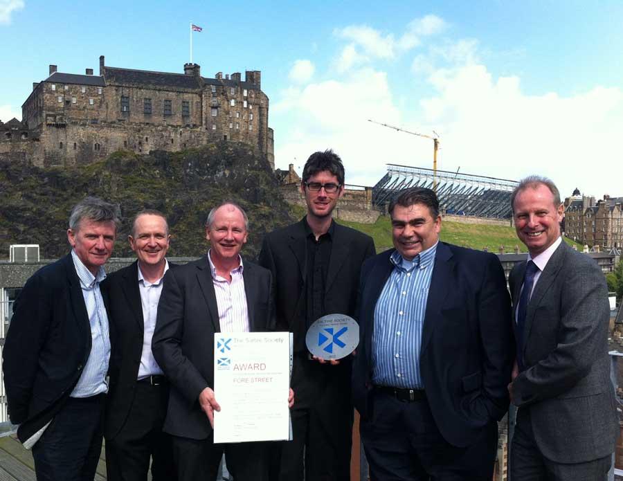 Design team holding Saltire Award in front of Edinburgh Castle